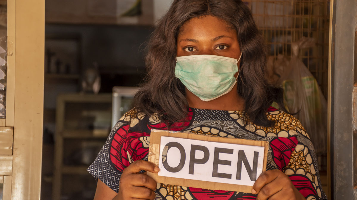 An African female entrepreneur wearing a mask stands in front of her store