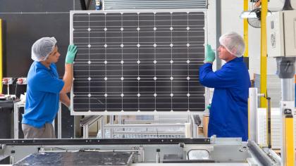 Factory workers lifting new solar panel from production line